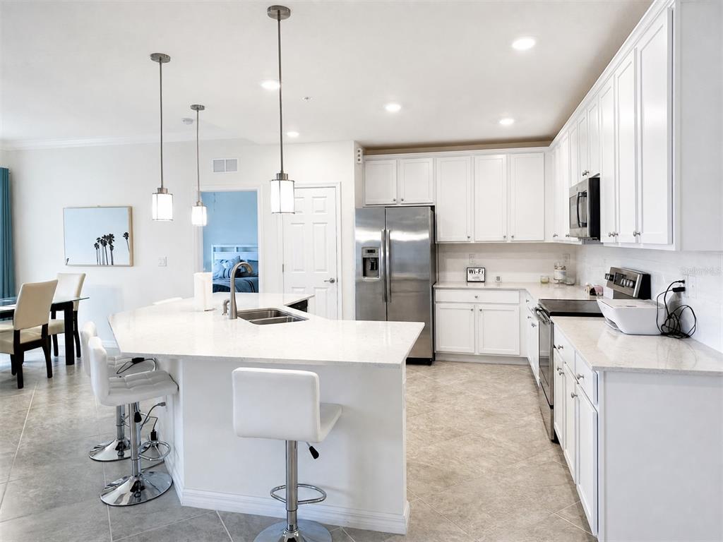 A modern kitchen features white cabinetry, stainless steel appliances, and a large quartz-topped island — 10054 CROOKED CREEK DRIVE UNIT 102, VENICE, FL