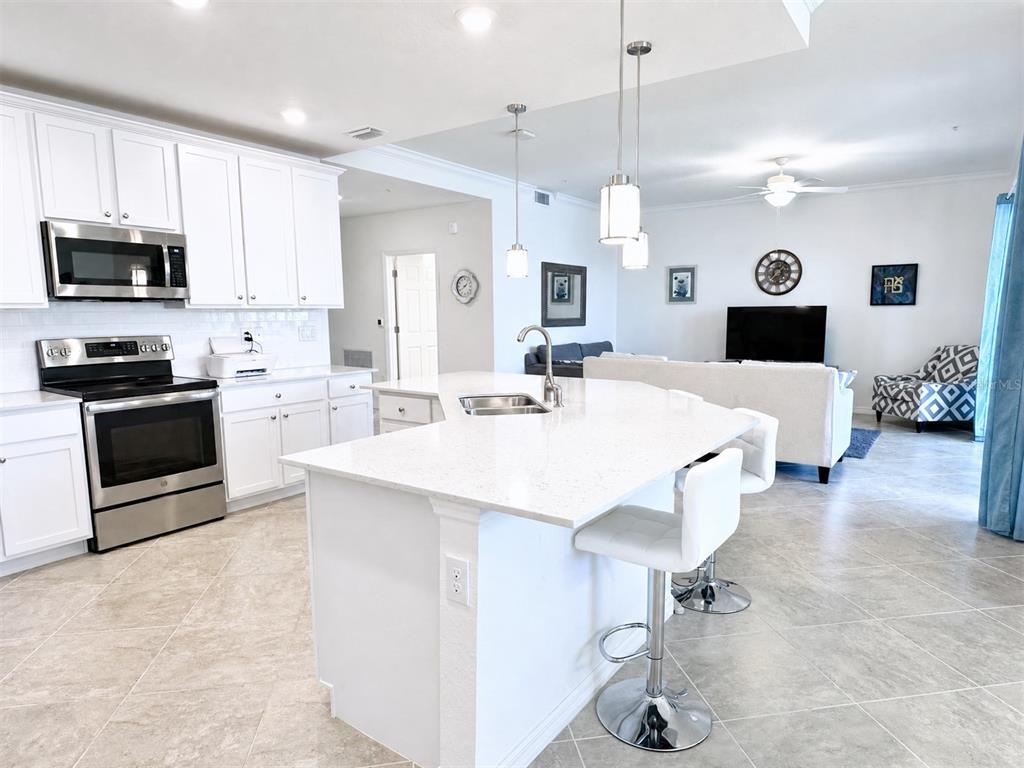 A white kitchen with a quartz island and stainless steel appliances opens to a living room — 10054 CROOKED CREEK DRIVE UNIT 102, VENICE, FL