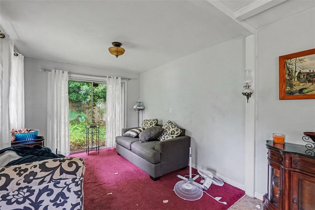 A living room features a gray sofa, magenta carpet, and a sliding glass door to greenery — 3220 GARDNER ROAD, LAKELAND, FL