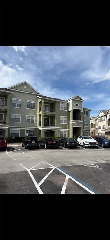 A multi-story apartment building with light green siding stands behind a paved parking lot — 8103 LILLIES WAY UNIT 108, ORLANDO, FL