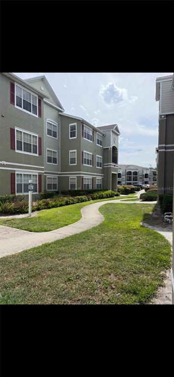 A multi-story apartment building with green siding and red shutters overlooks a curved walkway — 8103 LILLIES WAY UNIT 108, ORLANDO, FL