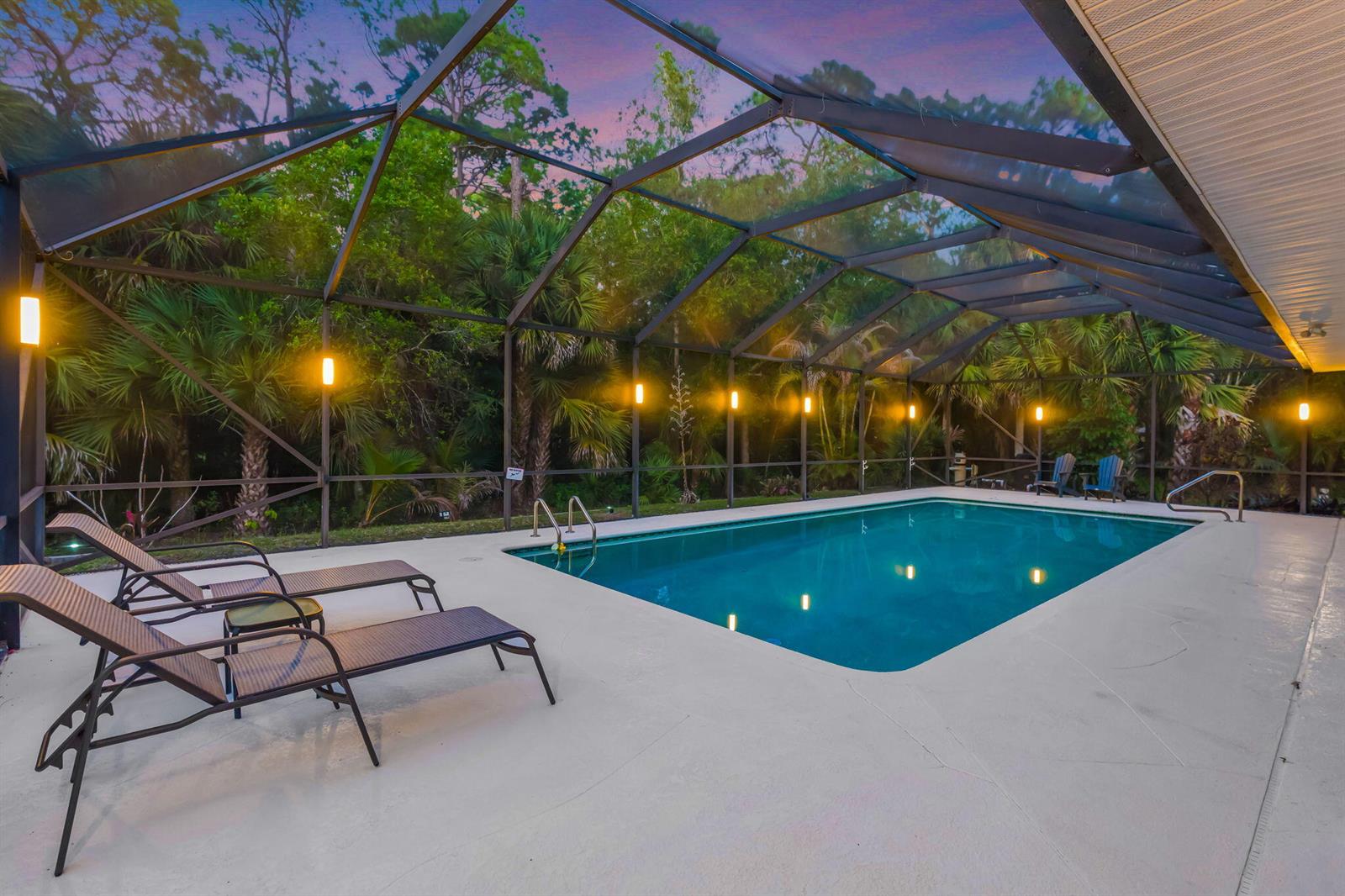 A swimming pool with lounge chairs is enclosed by a screened lanai at dusk — 9417 Whippoorwill Trail, FL 33478, FL