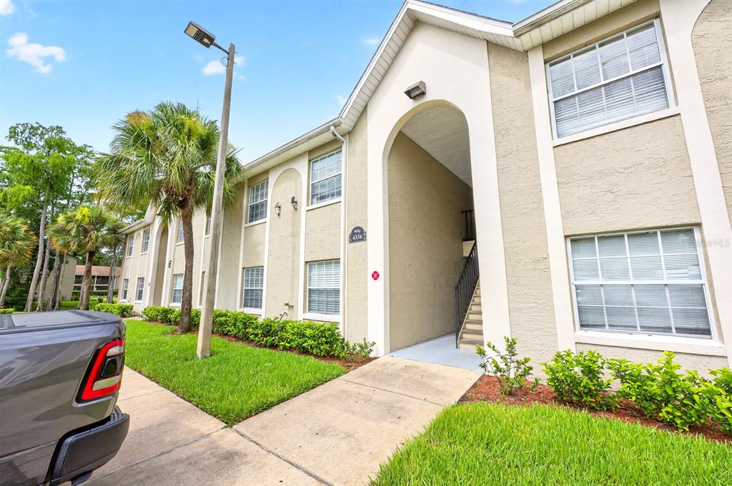 A multi-story apartment building exterior features beige stucco walls, white trim, and a covered entryway — 4336 HECTOR COURT UNIT 7, ORLANDO, FL