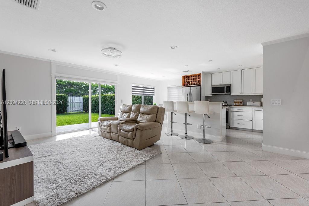 An open-concept living room and kitchen feature white cabinetry, tile flooring, and sliding glass doors — 6256 Lansdowne Cir, Boynton Beach FL 33472, BOYNTON BEACH, FL