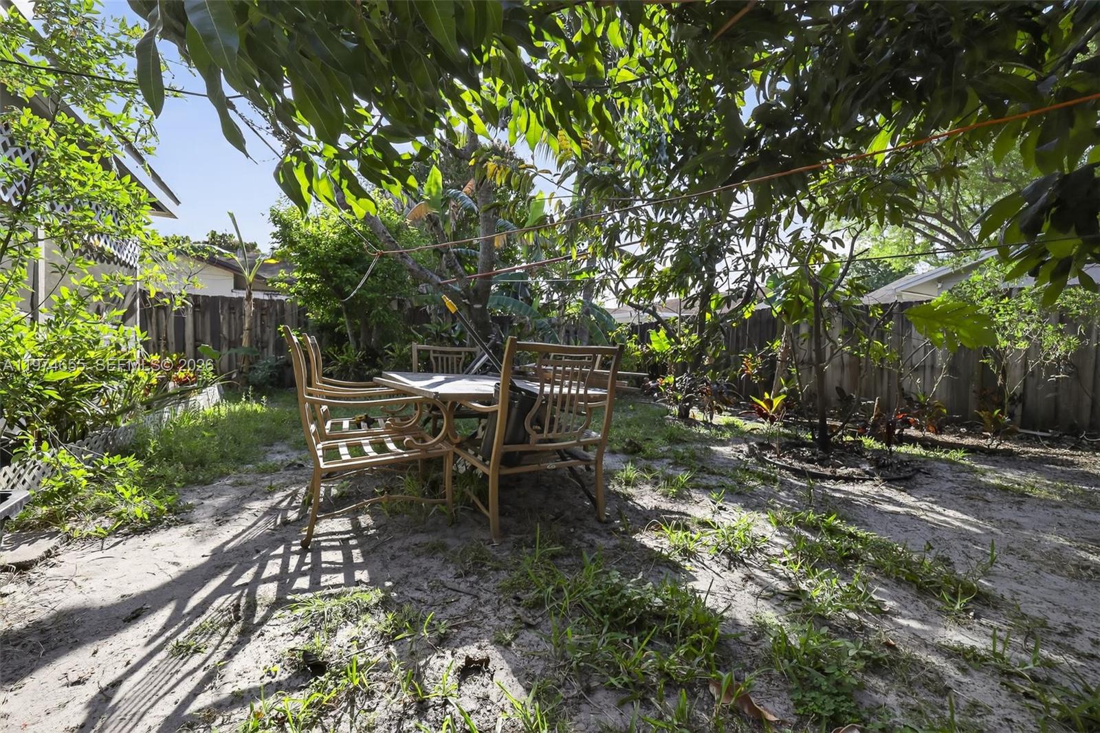 A metal patio table and chairs sit on a sandy backyard lawn under trees — 9522 Affirmed Ln, Boca Raton FL 33496, BOCA RATON, FL