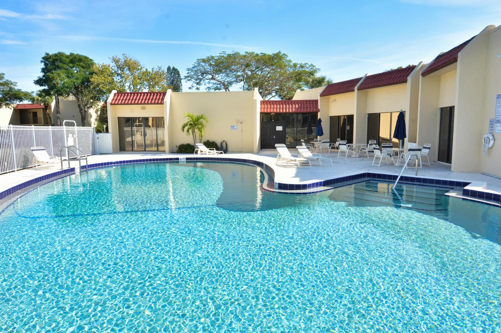A swimming pool with a surrounding patio and lounge chairs sits in front of apartment buildings — 2050 Oleander Boulevard # 306, Fort Pierce FL 34950, FORT PIERCE, FL