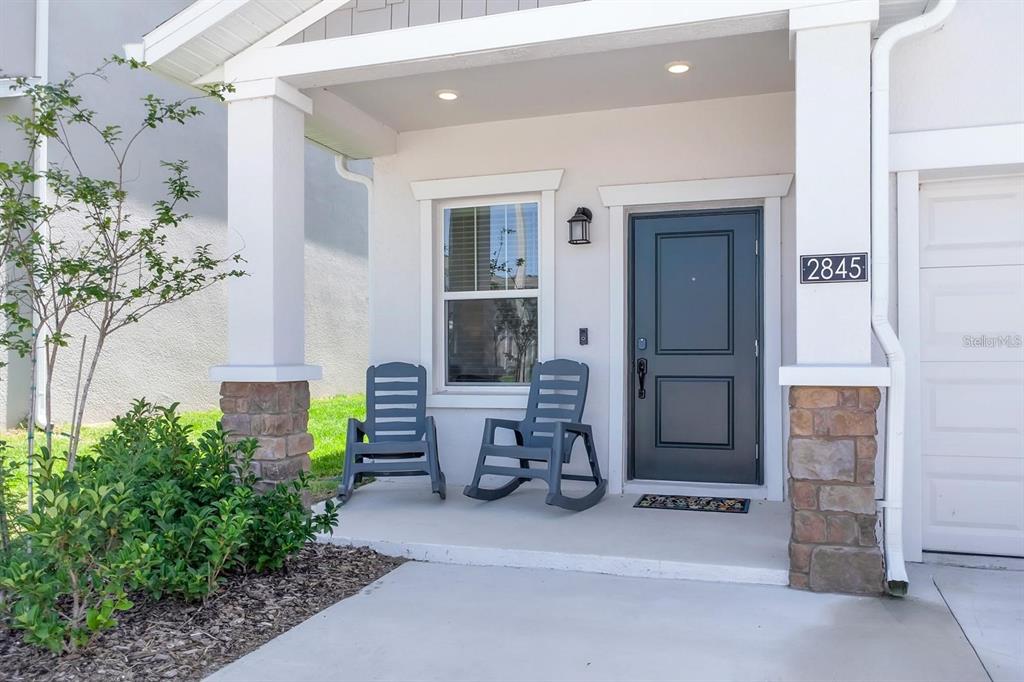 A covered front porch features two gray rocking chairs, a dark door, and stone accents — 2845 PIERR STREET, DAVENPORT, FL