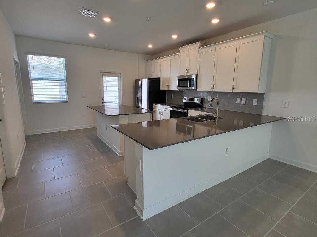 A kitchen features white cabinets, dark countertops, stainless steel appliances, and gray tile flooring — 11239 LISTENING DRIVE, ORLANDO, FL