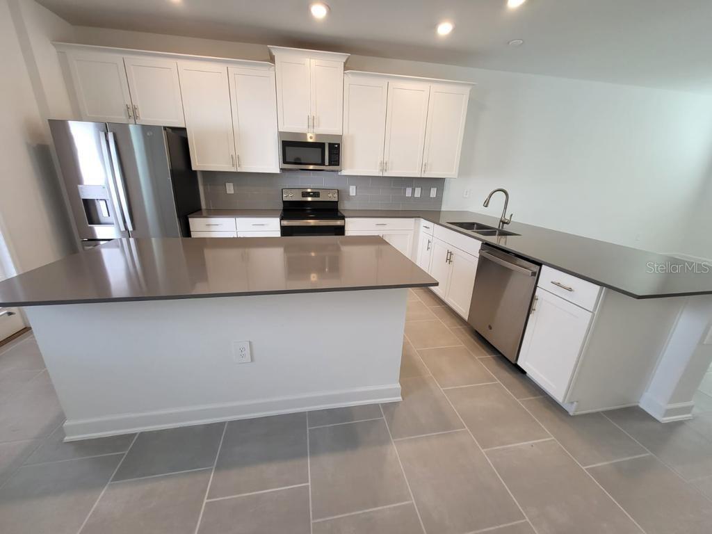 A modern kitchen features white cabinets, gray countertops, stainless steel appliances, and tile flooring — 11239 LISTENING DRIVE, ORLANDO, FL
