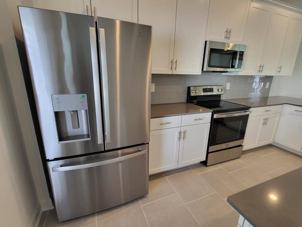 A kitchen features stainless steel appliances, white cabinets, gray countertops, and light tile flooring — 11239 LISTENING DRIVE, ORLANDO, FL