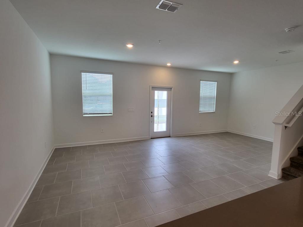 An empty living room features light gray tile flooring, white walls, and a glass-paneled door — 11239 LISTENING DRIVE, ORLANDO, FL