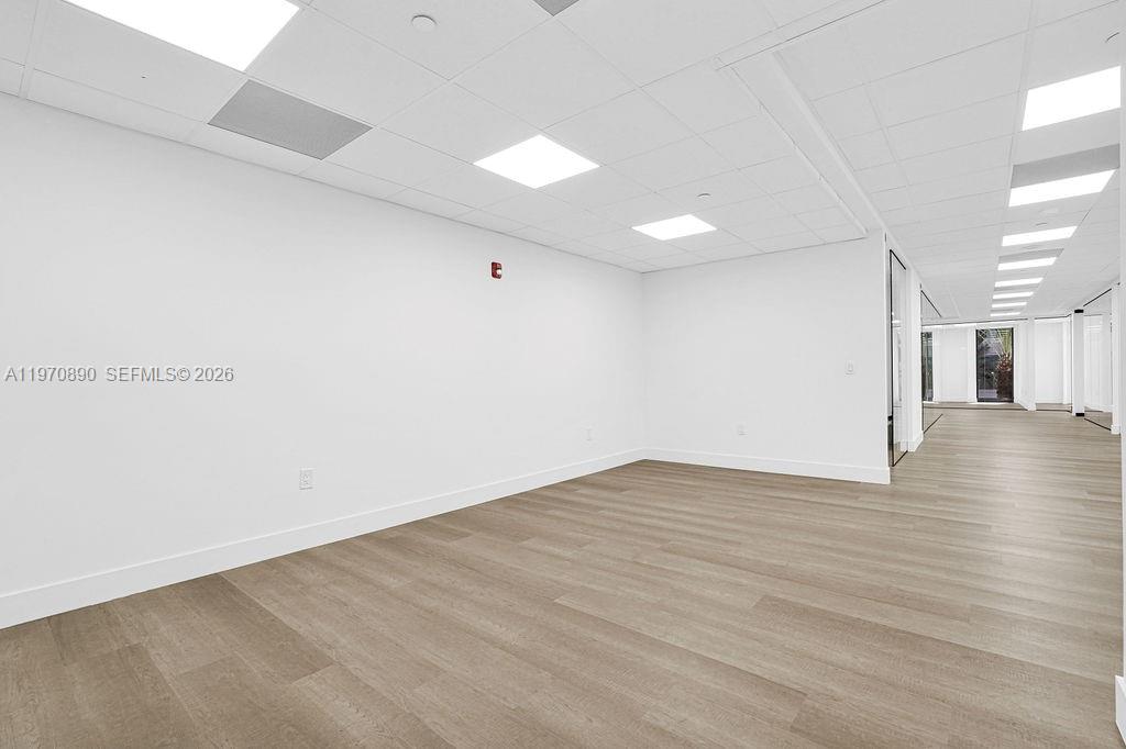 An empty office space features white walls, a drop ceiling with recessed lighting, and wood-look flooring — 1110 Brickell Ave # 310A, Miami FL 33131, MIAMI, FL