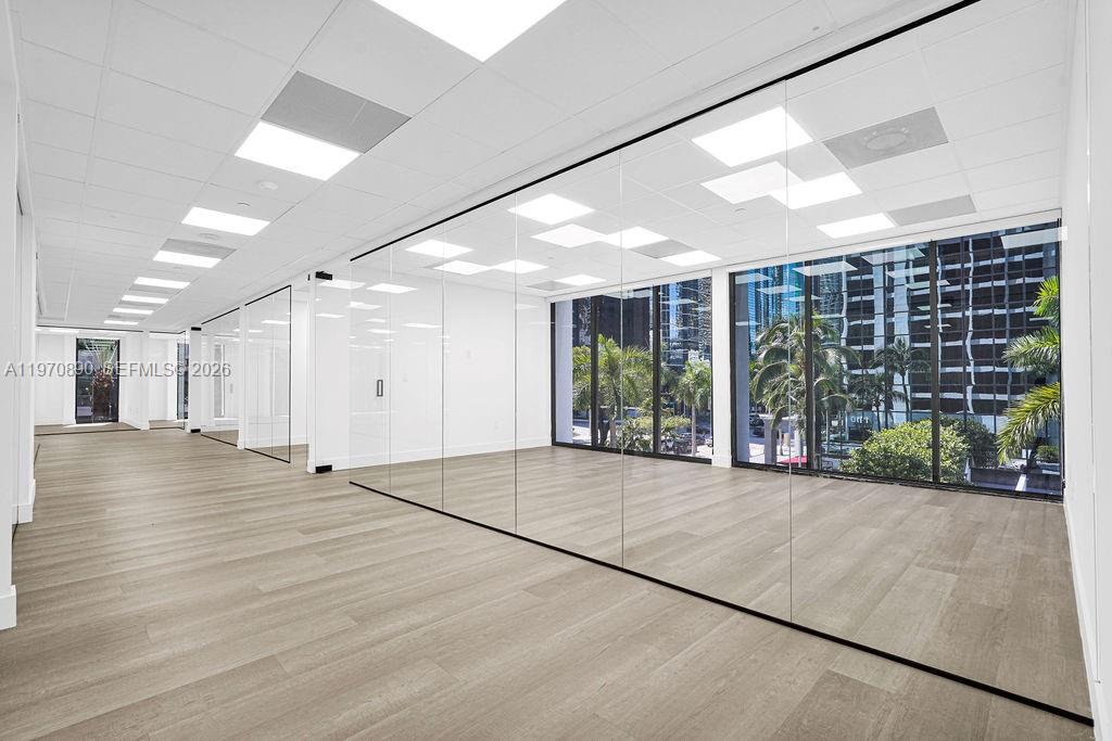 An empty office space features glass partitions, recessed lighting, and light wood-look flooring — 1110 Brickell Ave # 310A, Miami FL 33131, MIAMI, FL