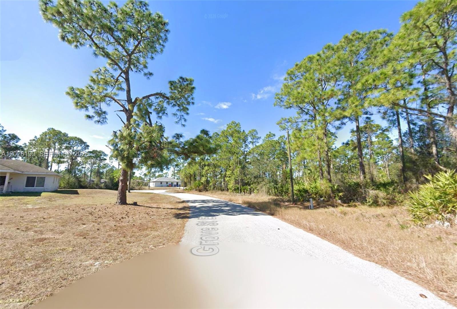 A gravel road winds through a wooded residential area with scattered houses — 1047 Grove St E, Lehigh Acres FL 33974, LEHIGH ACRES, FL