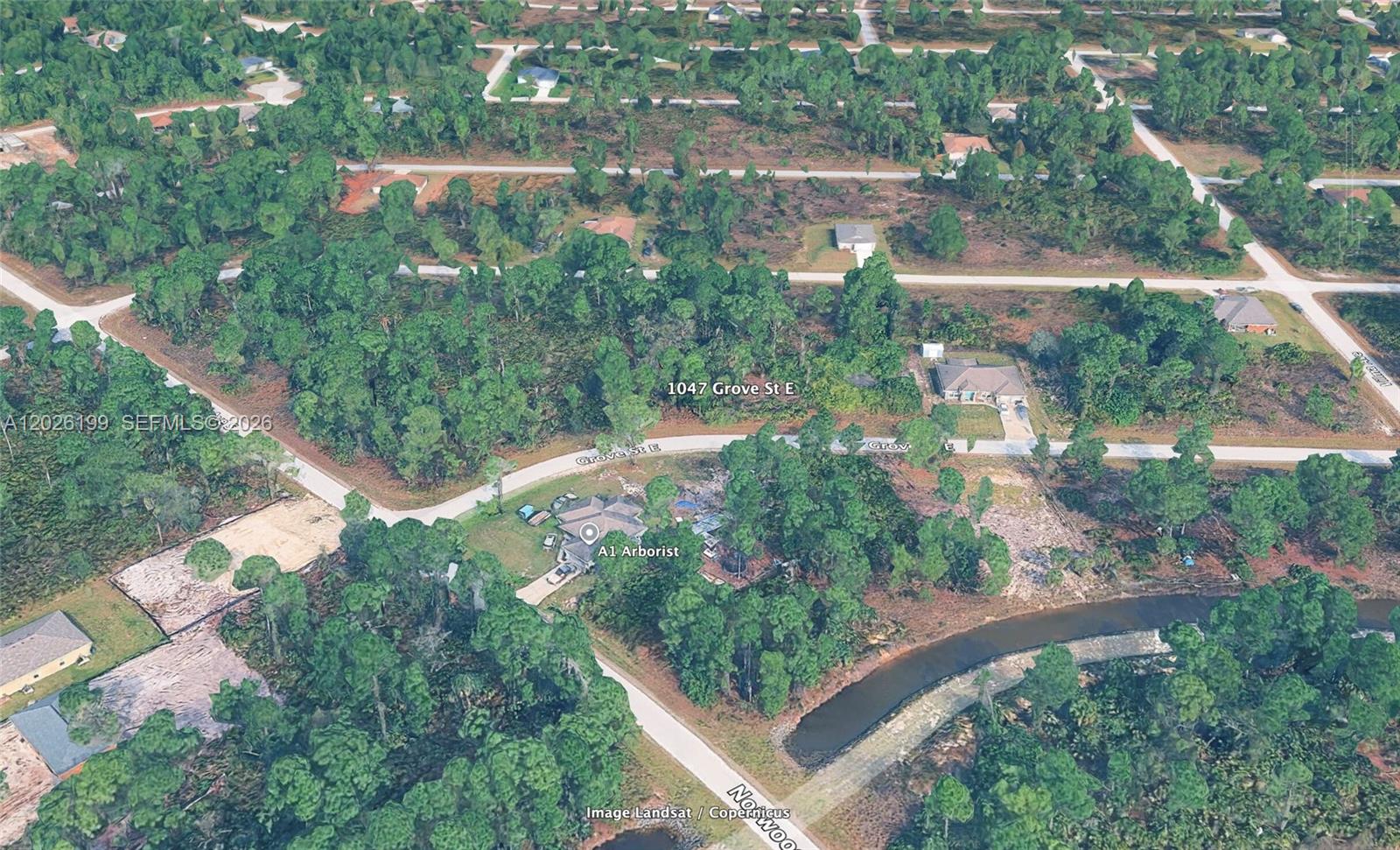 This aerial view shows a residential property with a house and trees near a canal — 1047 Grove St E, Lehigh Acres FL 33974, LEHIGH ACRES, FL