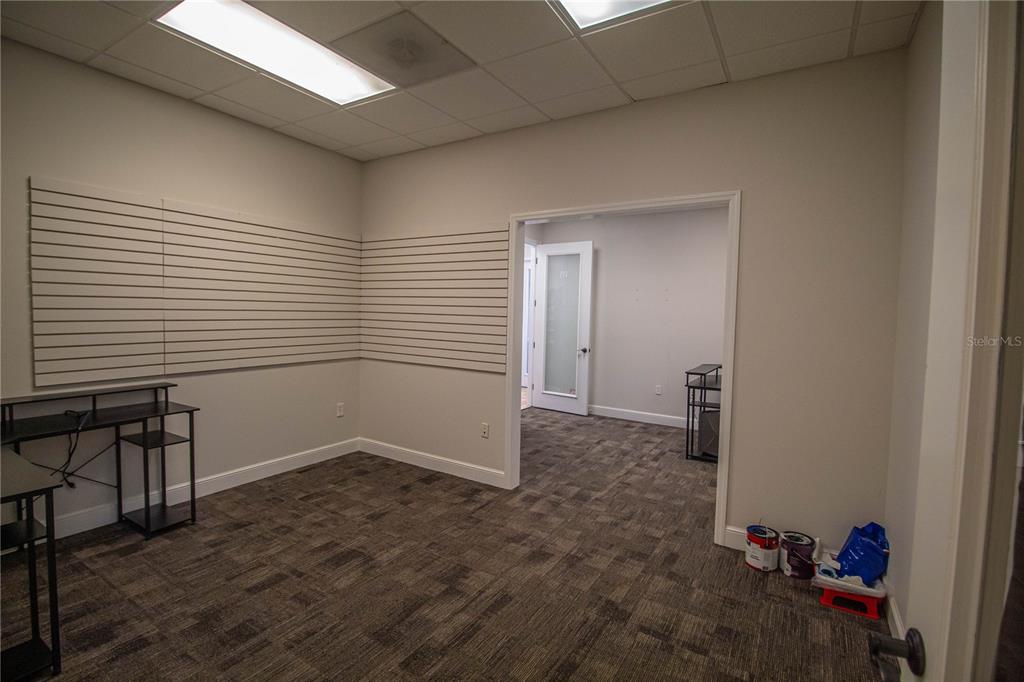 An office space features slat walls, a dark carpet, and an open doorway to another room — 252 W MARION AVENUE UNIT 113 & 115, PUNTA GORDA, FL