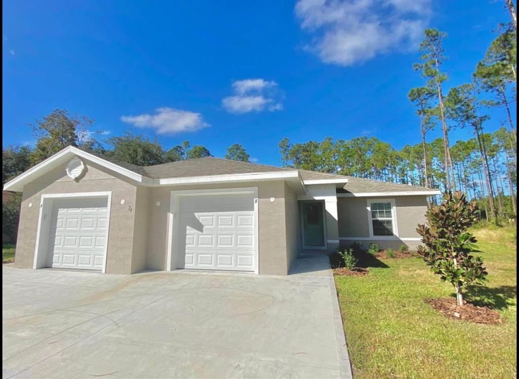 A single-story duplex with two garage doors, beige stucco siding, and a concrete driveway — 74 EMERSON DRIVE UNIT A & B, PALM COAST, FL