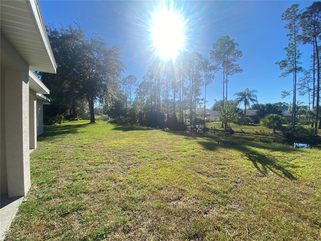 A view of a grassy backyard with trees, a small pond, and a house exterior — 74 EMERSON DRIVE UNIT A & B, PALM COAST, FL