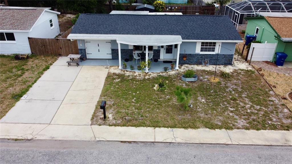 An aerial view shows a single-story house with a gray roof, blue siding, and a driveway — 1421 WICKHAM LANE, HOLIDAY, FL