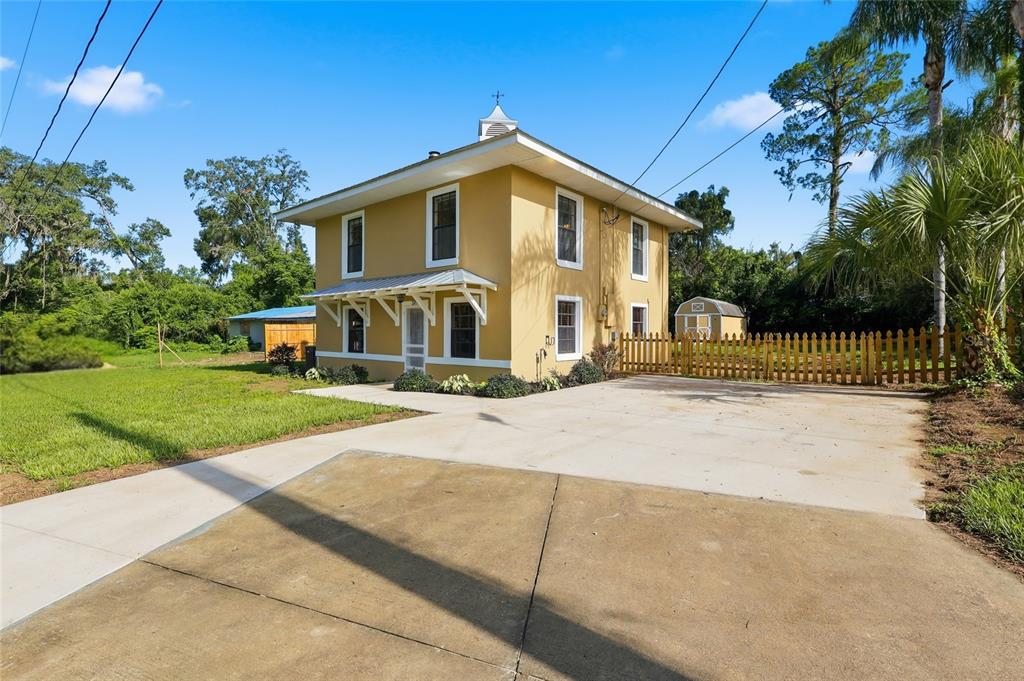 A two-story yellow house with a white trim and a concrete driveway sits on grass — 37715 DIXIE AVENUE, DADE CITY, FL