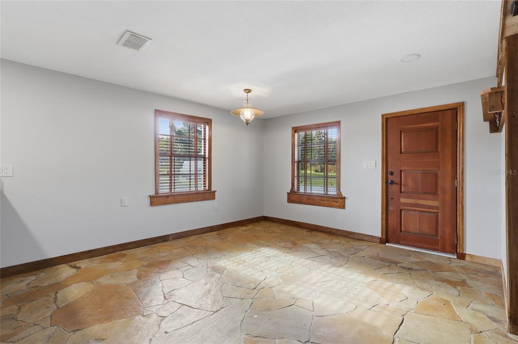 An empty room features light gray walls, a flagstone floor, and a wooden front door — 37715 DIXIE AVENUE, DADE CITY, FL