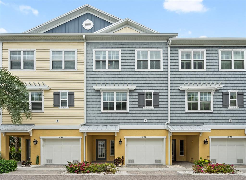 A three-story townhouse exterior features yellow and blue siding with three attached garage doors — 3162 MOORINGS DRIVE, ST PETERSBURG, FL