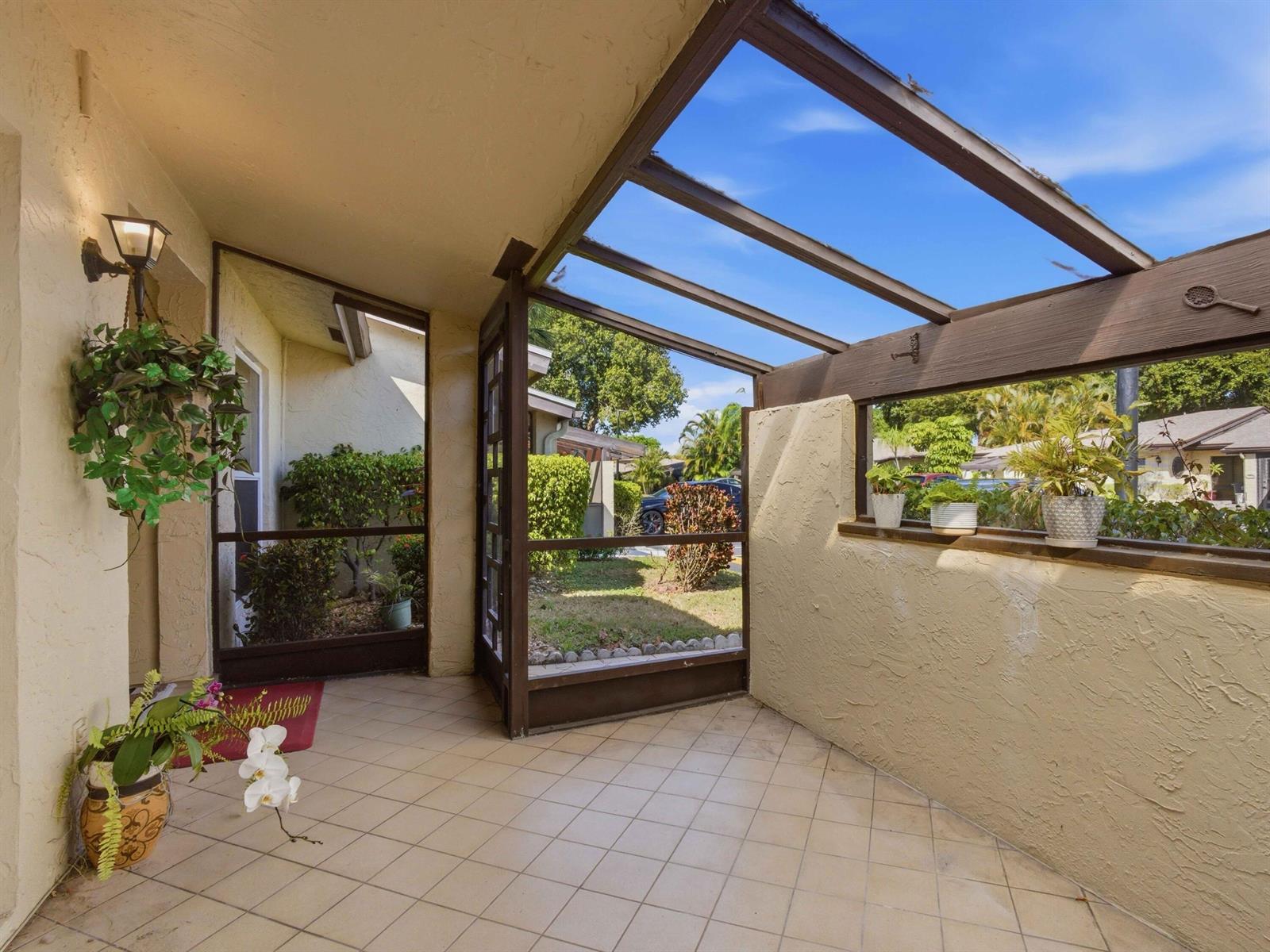 A covered, screened-in patio with tiled flooring, a glass roof, and potted plants — 13773 Via Aurora # C, Delray Beach FL 33484, DELRAY BEACH, FL