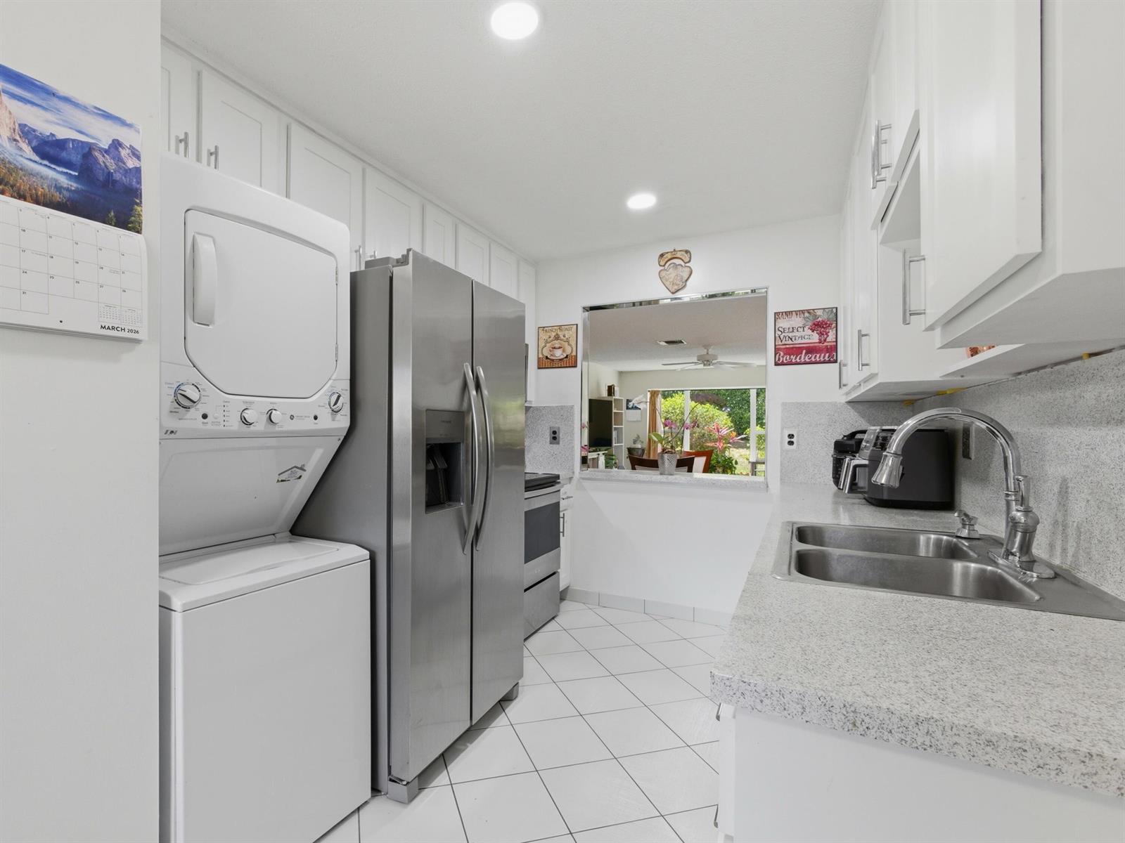 A kitchen features white cabinets, stainless steel appliances, a stacked washer-dryer, and a pass-through window — 13773 Via Aurora # C, Delray Beach FL 33484, DELRAY BEACH, FL