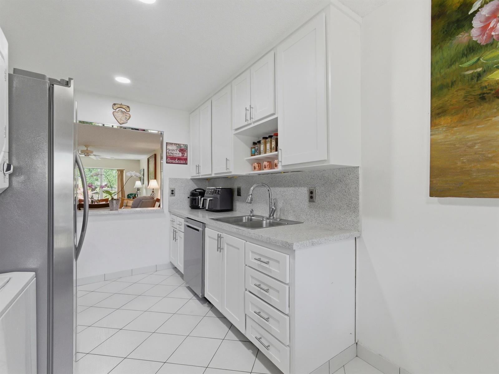 A kitchen features white cabinets, granite countertops, stainless steel appliances, and a pass-through window — 13773 Via Aurora # C, Delray Beach FL 33484, DELRAY BEACH, FL