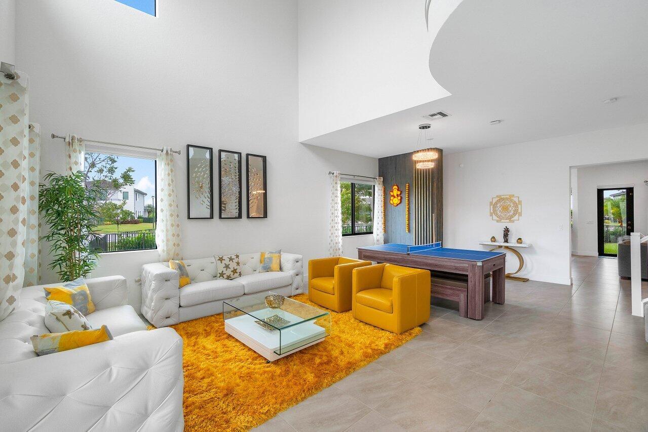 A bright living room features white sofas, yellow armchairs, a shag rug, and a ping-pong table — 10780 Oceano Way, Parkland FL 33076, PARKLAND, FL