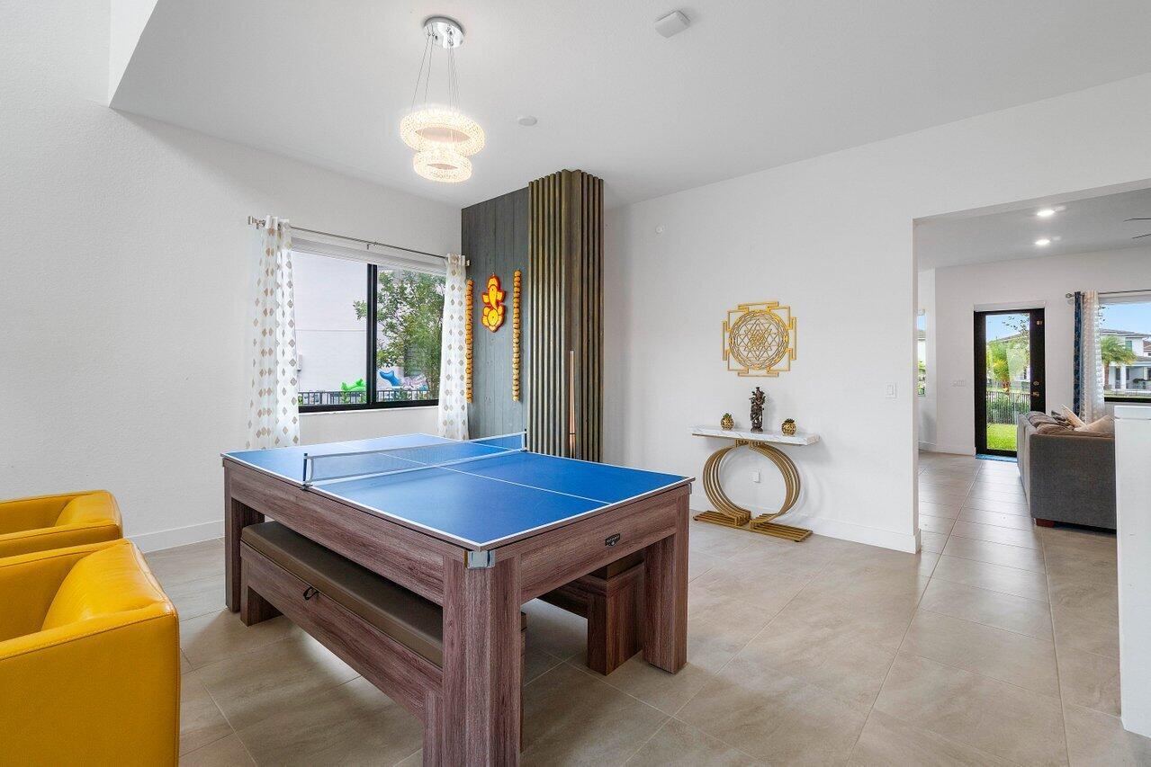 A game room features a blue ping pong table, yellow chairs, and a modern chandelier — 10780 Oceano Way, Parkland FL 33076, PARKLAND, FL