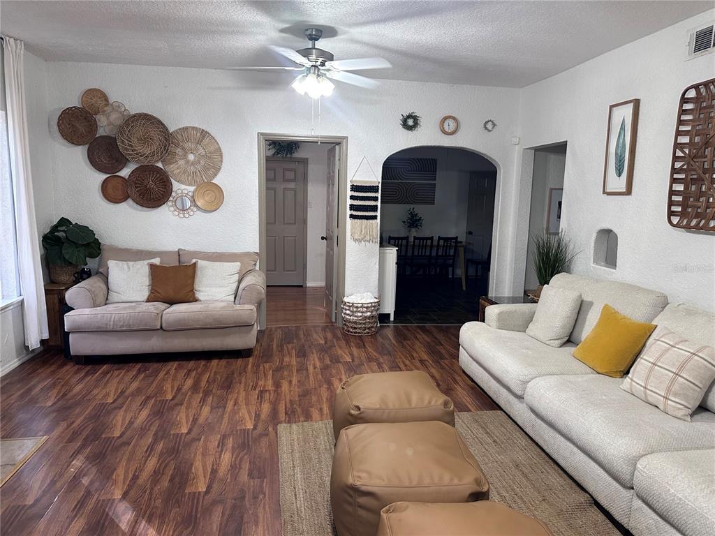 A living room features two sofas, leather ottomans, wood-look flooring, and wall-mounted woven decor — 1910 WILLIAM CLARK AVENUE, SANFORD, FL