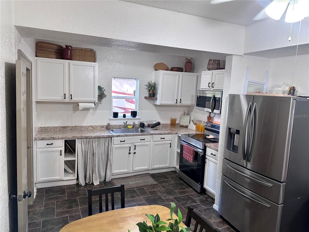 A kitchen features white cabinets, stainless steel appliances, a laminate countertop, and dark tile flooring — 1910 WILLIAM CLARK AVENUE, SANFORD, FL