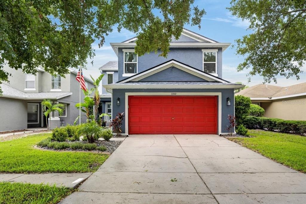 A two-story blue house features a prominent red garage door and a concrete driveway — 11342 COCOA BEACH DRIVE, RIVERVIEW, FL