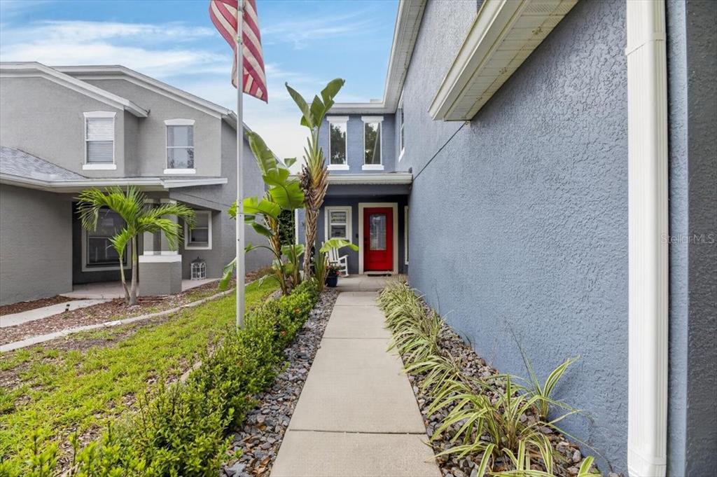 A concrete walkway leads to a red front door between two blue-gray residential buildings — 11342 COCOA BEACH DRIVE, RIVERVIEW, FL