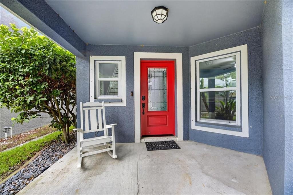 A covered porch features a red front door, a white rocking chair, and blue siding — 11342 COCOA BEACH DRIVE, RIVERVIEW, FL