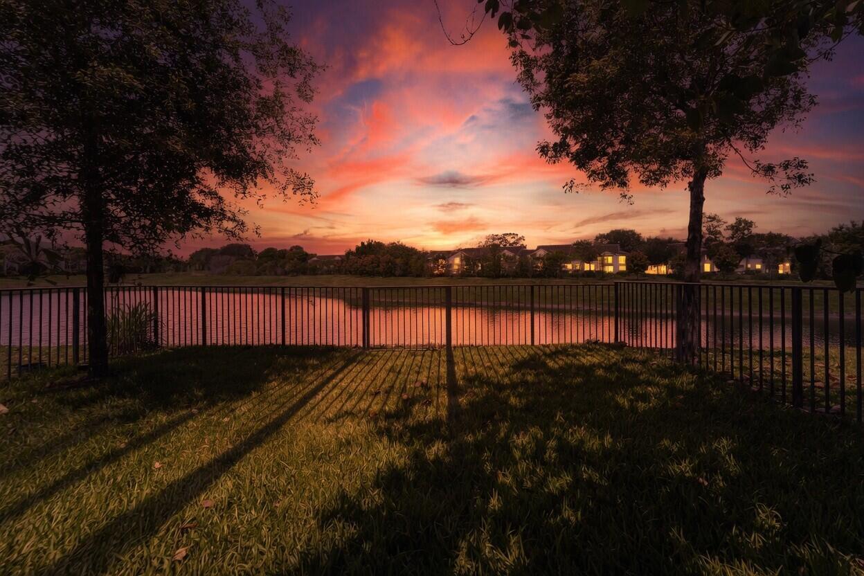 A backyard lawn with a metal fence overlooks a pond and houses at sunset — 295 NW 33rd Lane, Pompano Beach FL 33069, POMPANO BEACH, FL