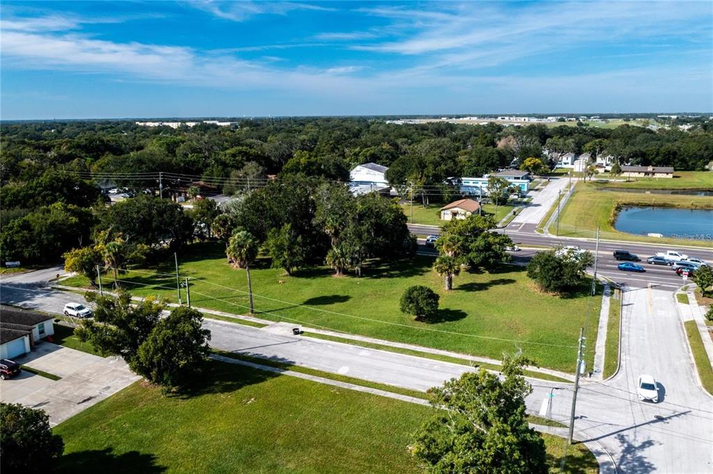 An aerial view shows a grassy vacant lot bordered by paved roads and mature trees — 0 JOHN YOUNG PARKWAY, KISSIMMEE, FL