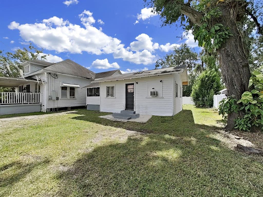 A white wood-sided house with a dark door and a large tree in the yard — 601 W BAKER STREET, PLANT CITY, FL