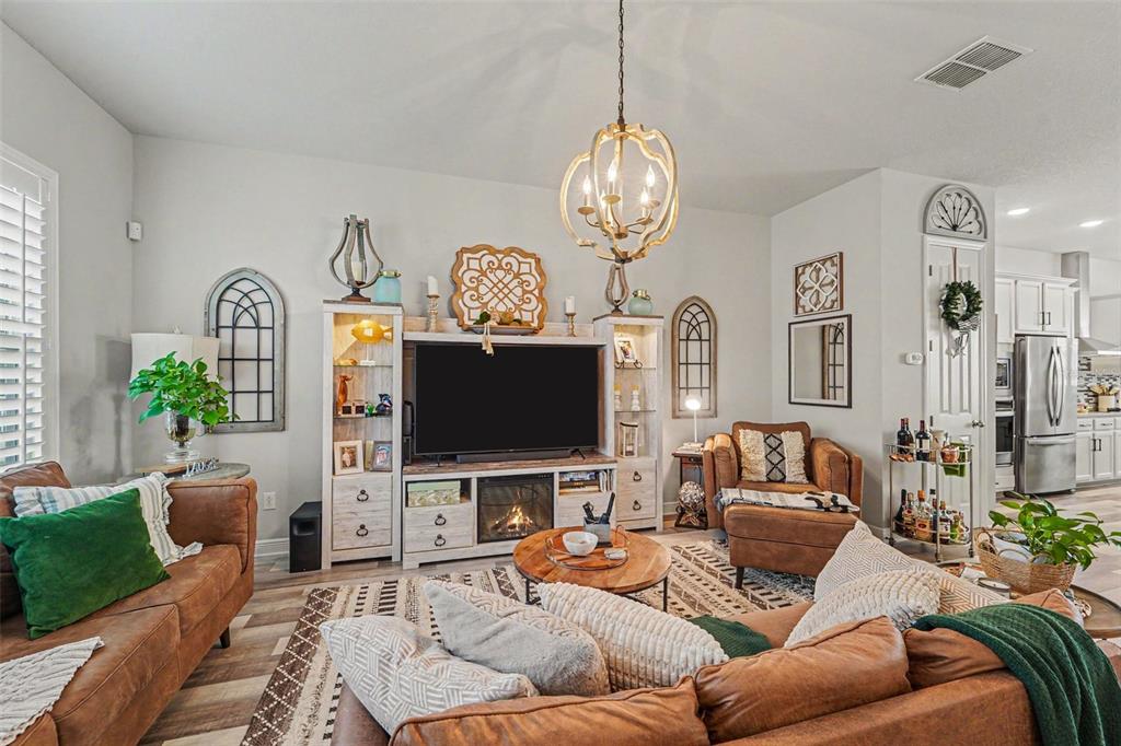A living room features leather furniture, a fireplace media console, and a rustic chandelier — 9567 CAVENDISH DRIVE, TAMPA, FL