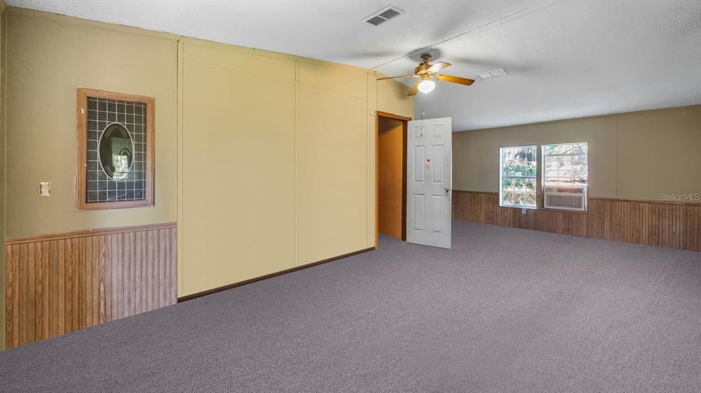 A carpeted room features paneled walls, a ceiling fan, and a window with an air conditioner — 23158 LOOP ROAD, GROVELAND, FL