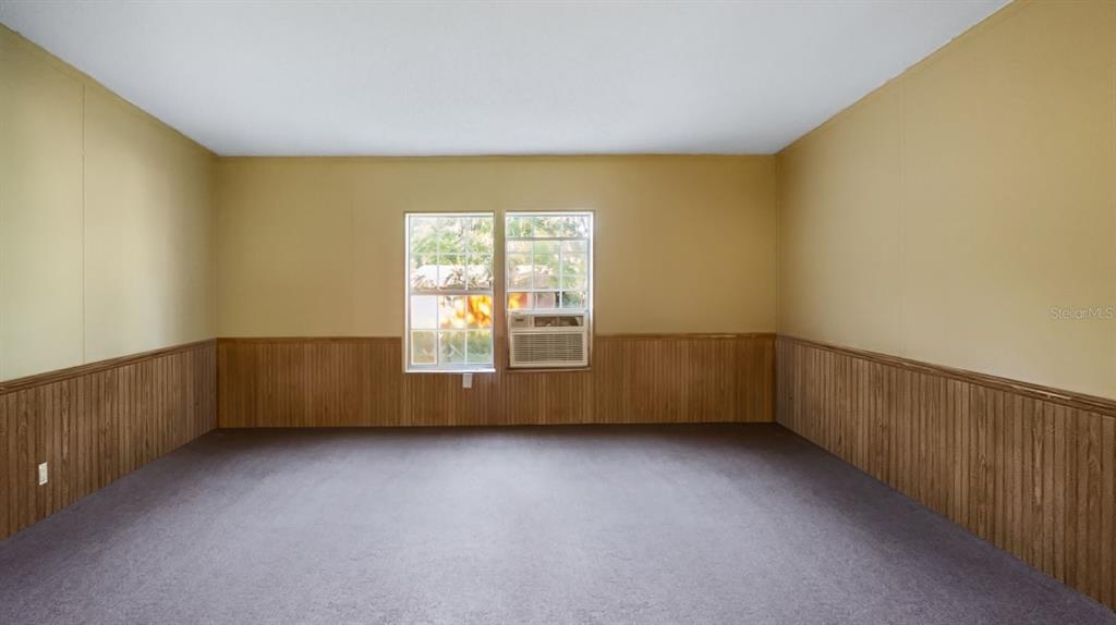 An empty room features wood paneling on the lower walls, carpeted flooring, and a window unit — 23158 LOOP ROAD, GROVELAND, FL