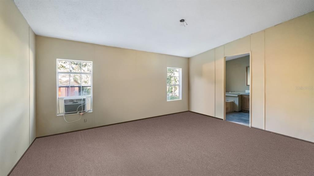 An empty bedroom features beige walls, brown carpeting, two windows, and an adjacent bathroom doorway — 23158 LOOP ROAD, GROVELAND, FL