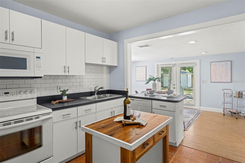 A kitchen features white cabinets, black countertops, a wooden island, and a view into a dining area — 3313 PRICE AVENUE, TAMPA, FL