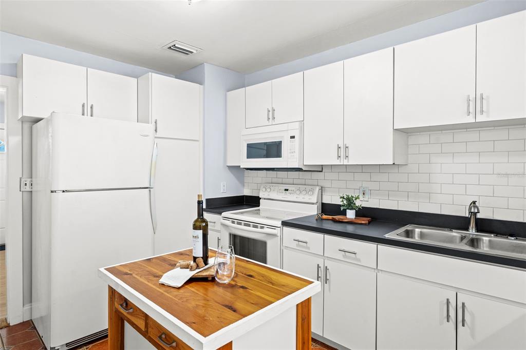 A kitchen features white cabinets, a black countertop, a subway tile backsplash, and a wooden island — 3313 PRICE AVENUE, TAMPA, FL