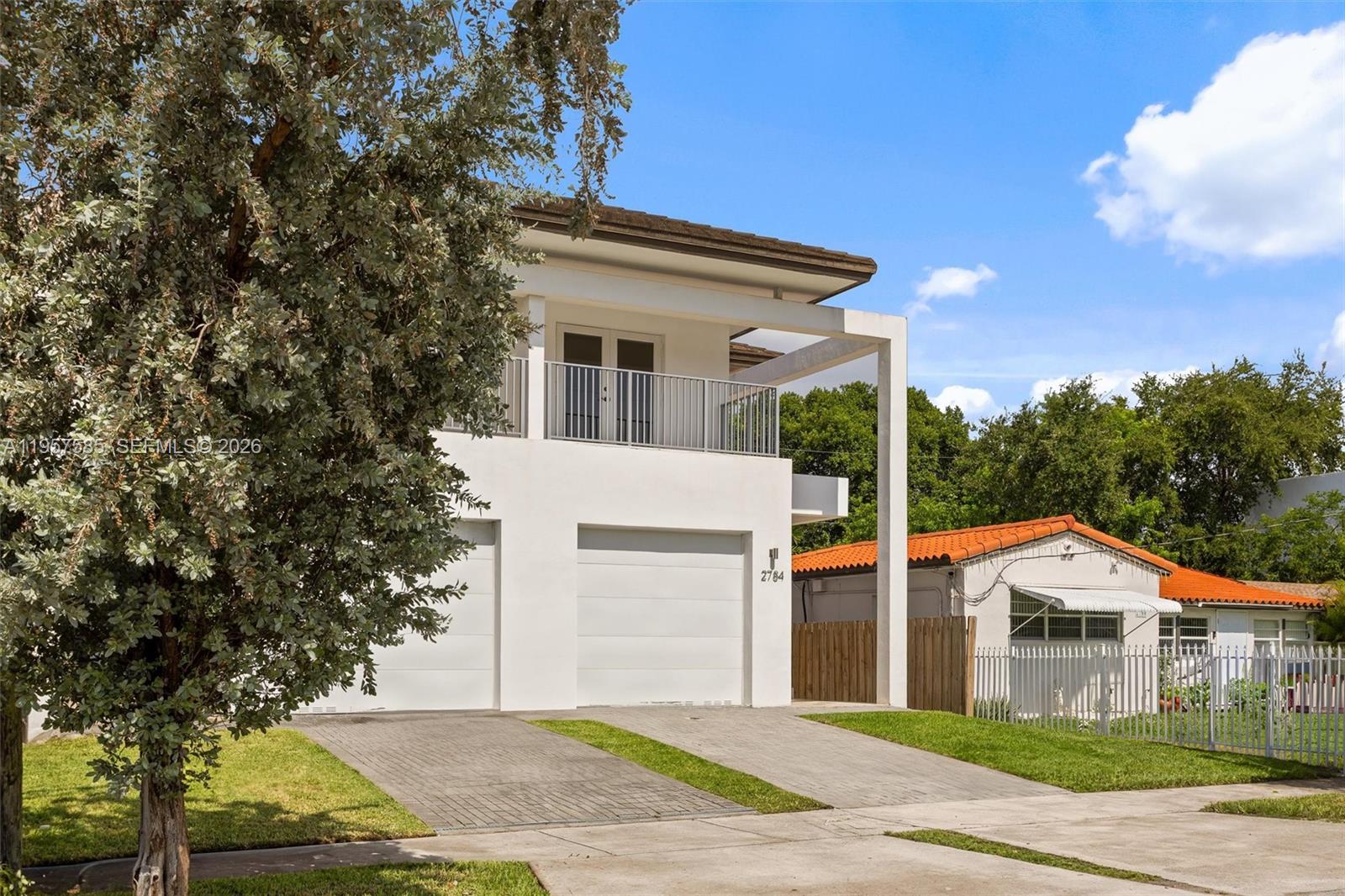 A two-story white modern house features a balcony, two garage doors, and a paved driveway — 2784 SW 34th Ave, Miami FL 33133, MIAMI, FL