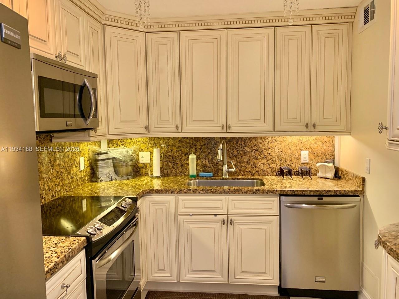 A kitchen features off-white cabinetry, granite countertops, stainless steel appliances, and an under-mount sink — 1985 S Ocean Dr # 3C, Hallandale Beach FL 33009, HALLANDALE BEACH, FL
