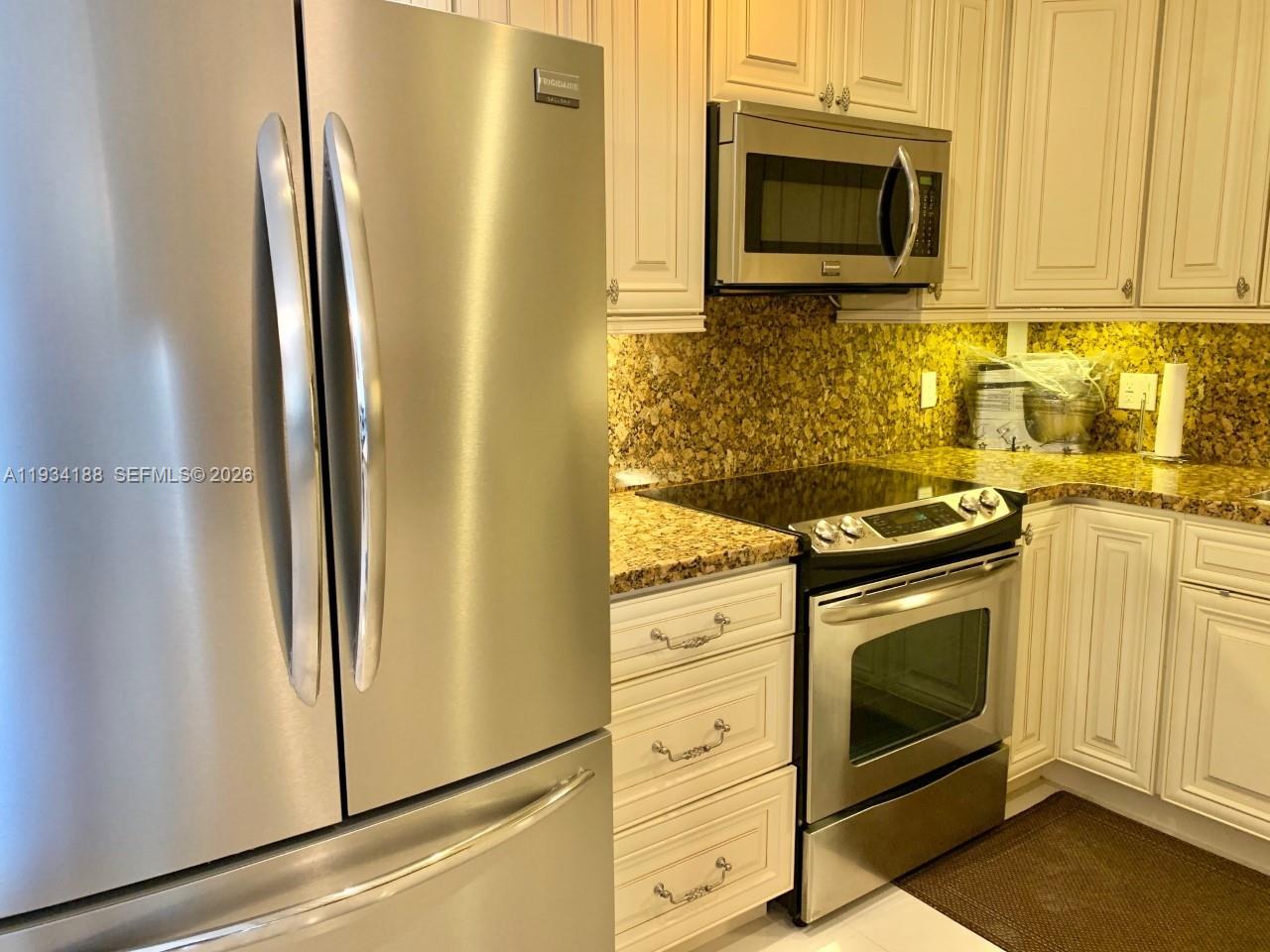 A kitchen features stainless steel appliances, off-white cabinets, and a speckled granite countertop — 1985 S Ocean Dr # 3C, Hallandale Beach FL 33009, HALLANDALE BEACH, FL