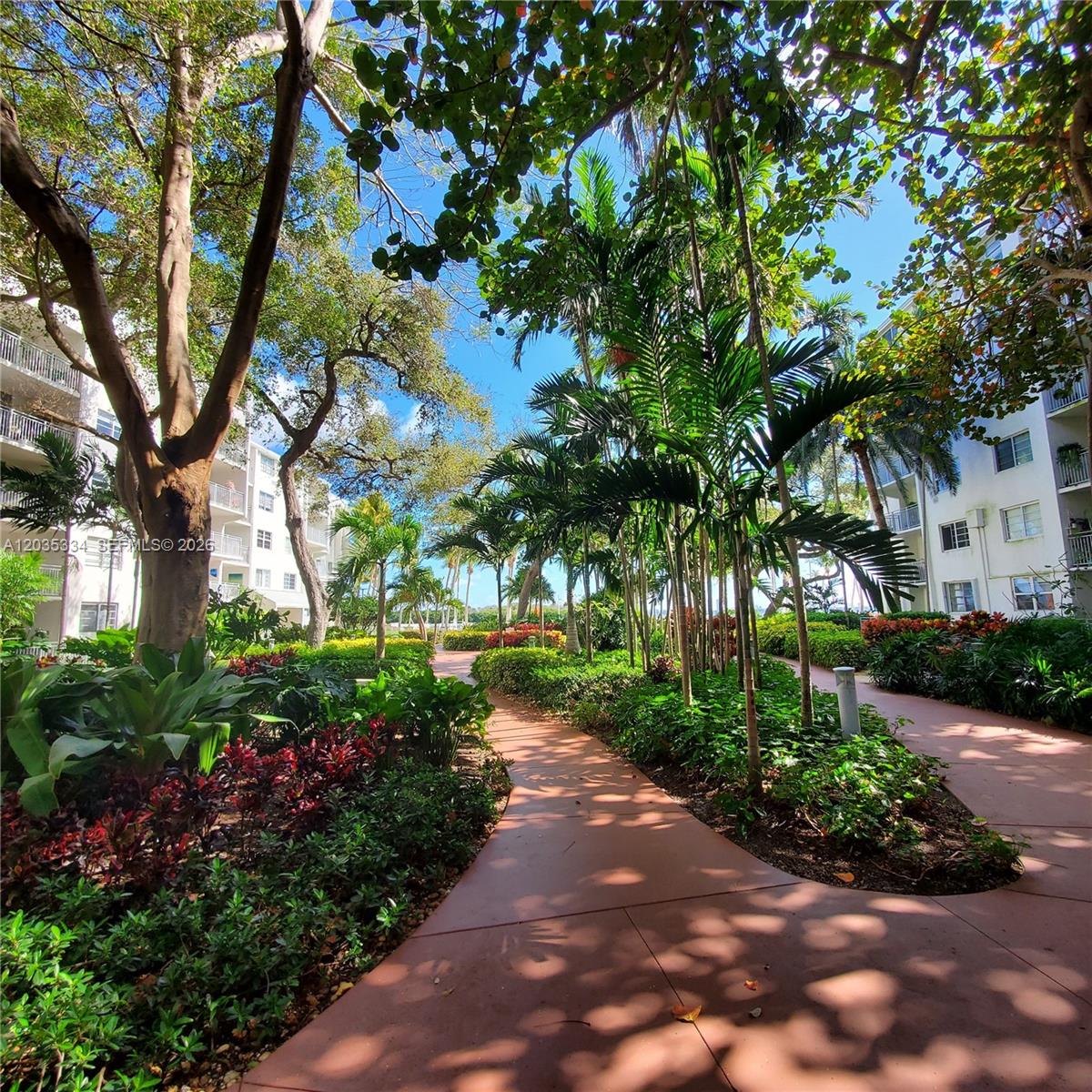 A paved walkway winds through a lush garden between two multi-story apartment buildings — 680 NE 64th St # A302, Miami FL 33138, MIAMI, FL