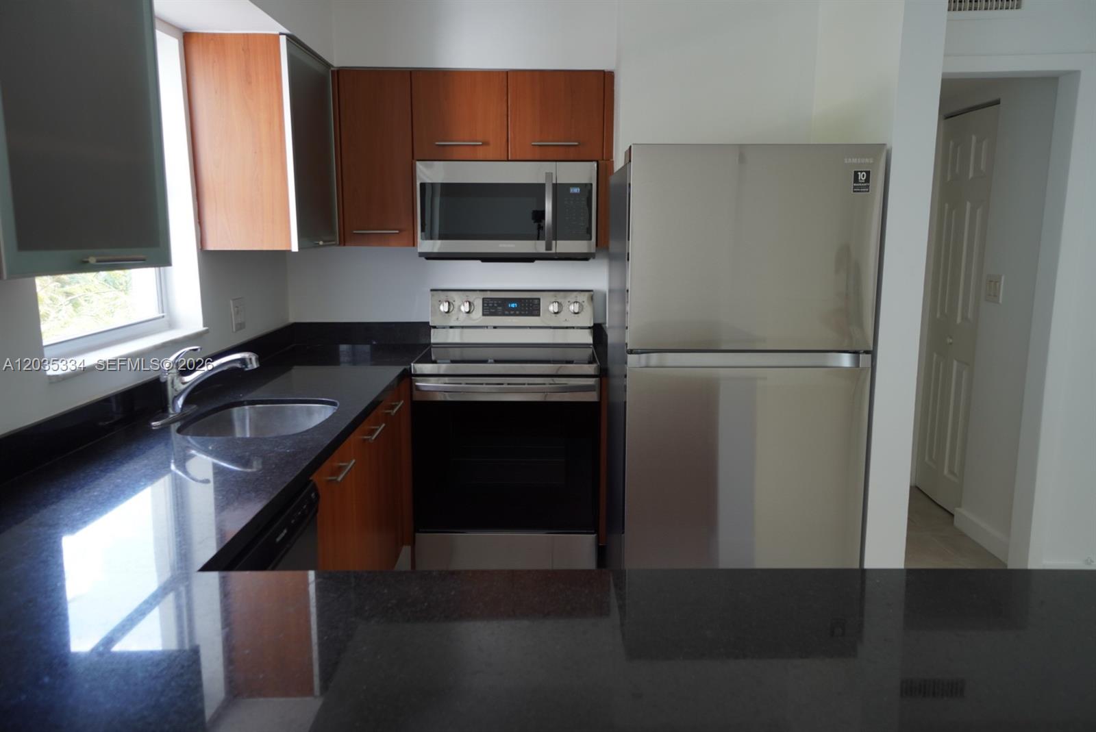 A kitchen features dark granite countertops, wood cabinets, and stainless steel appliances — 680 NE 64th St # A302, Miami FL 33138, MIAMI, FL